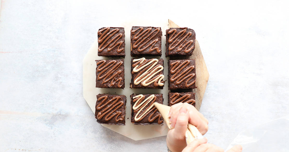 Decorating the top of brownie squares with a hazelnut and white chocolate spread. 
