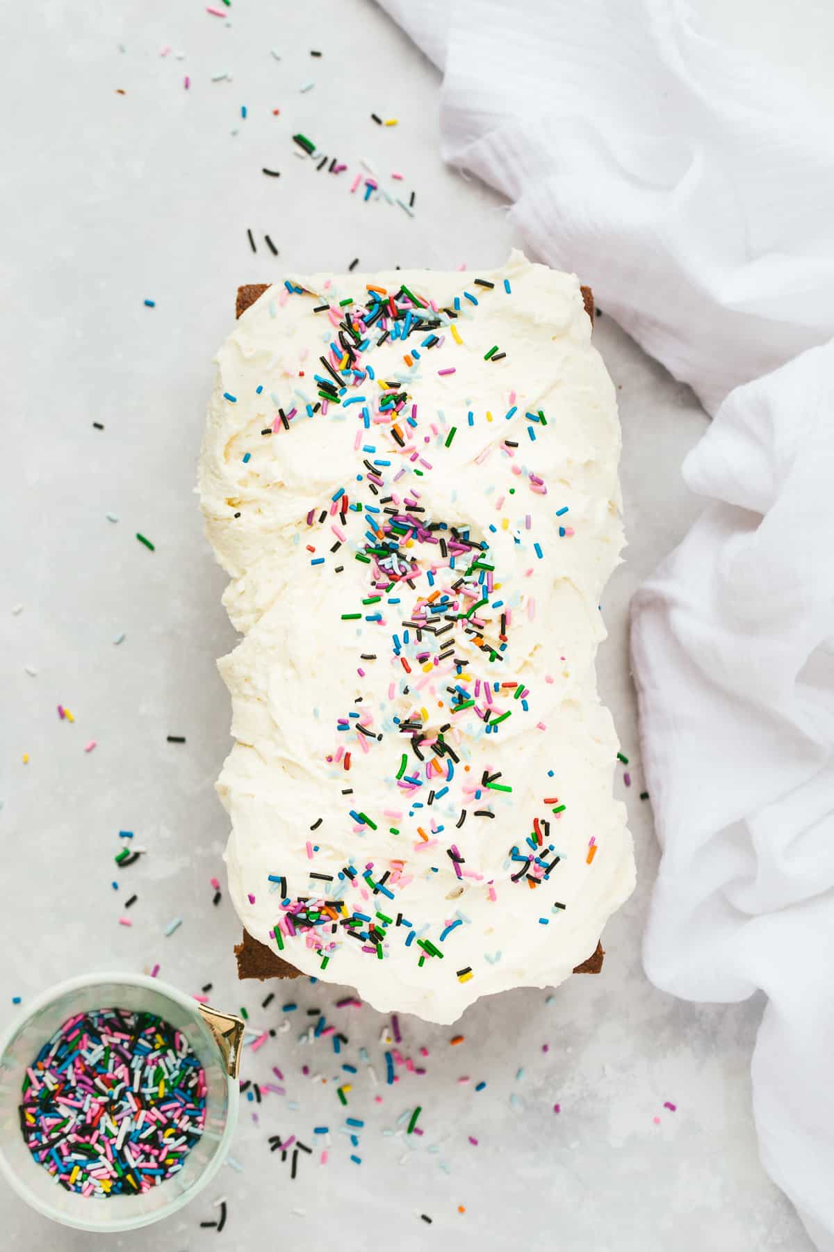 A Vanilla Loaf Cake that has been topped with vanilla buttercream icing and colourful sprinkles. 