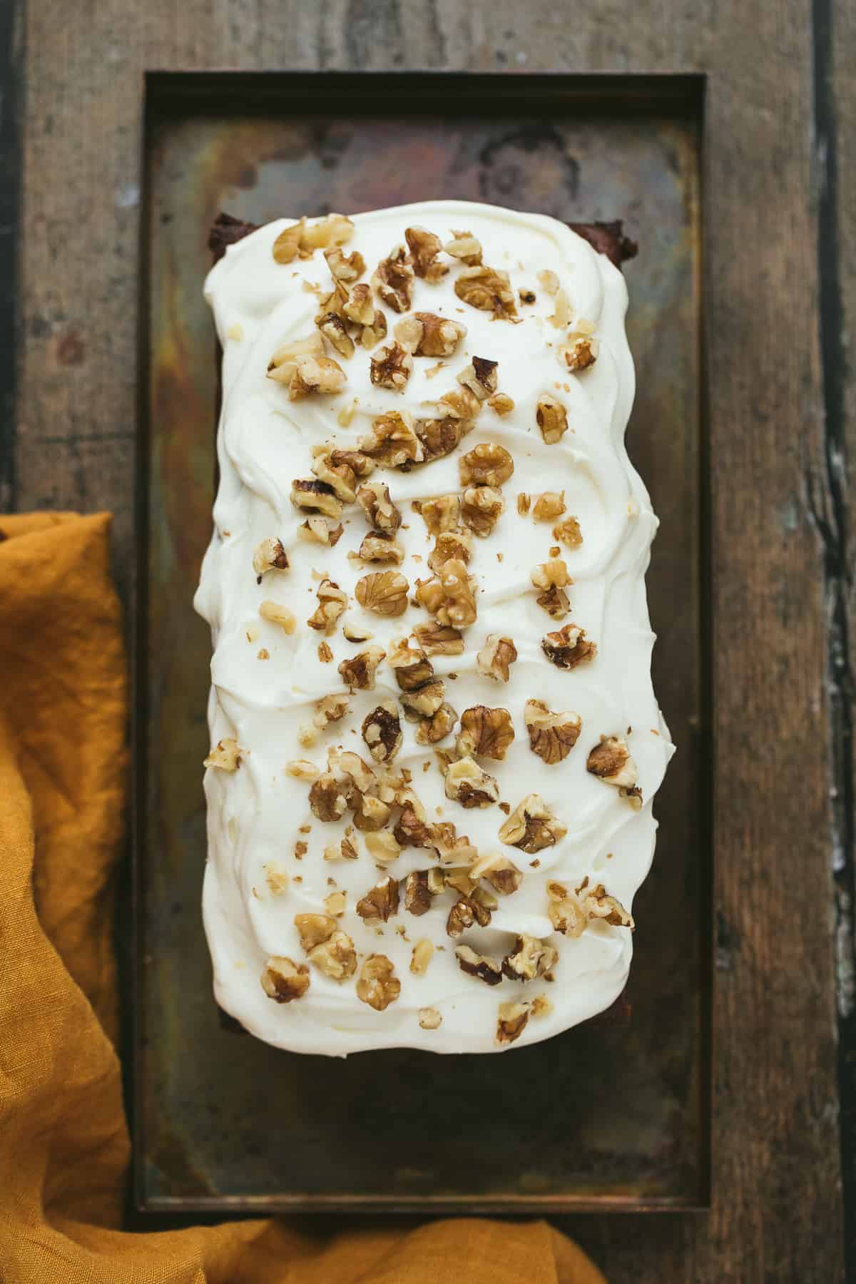 A loaf cake covered with cream cheese icing and topped with chopped walnuts. 