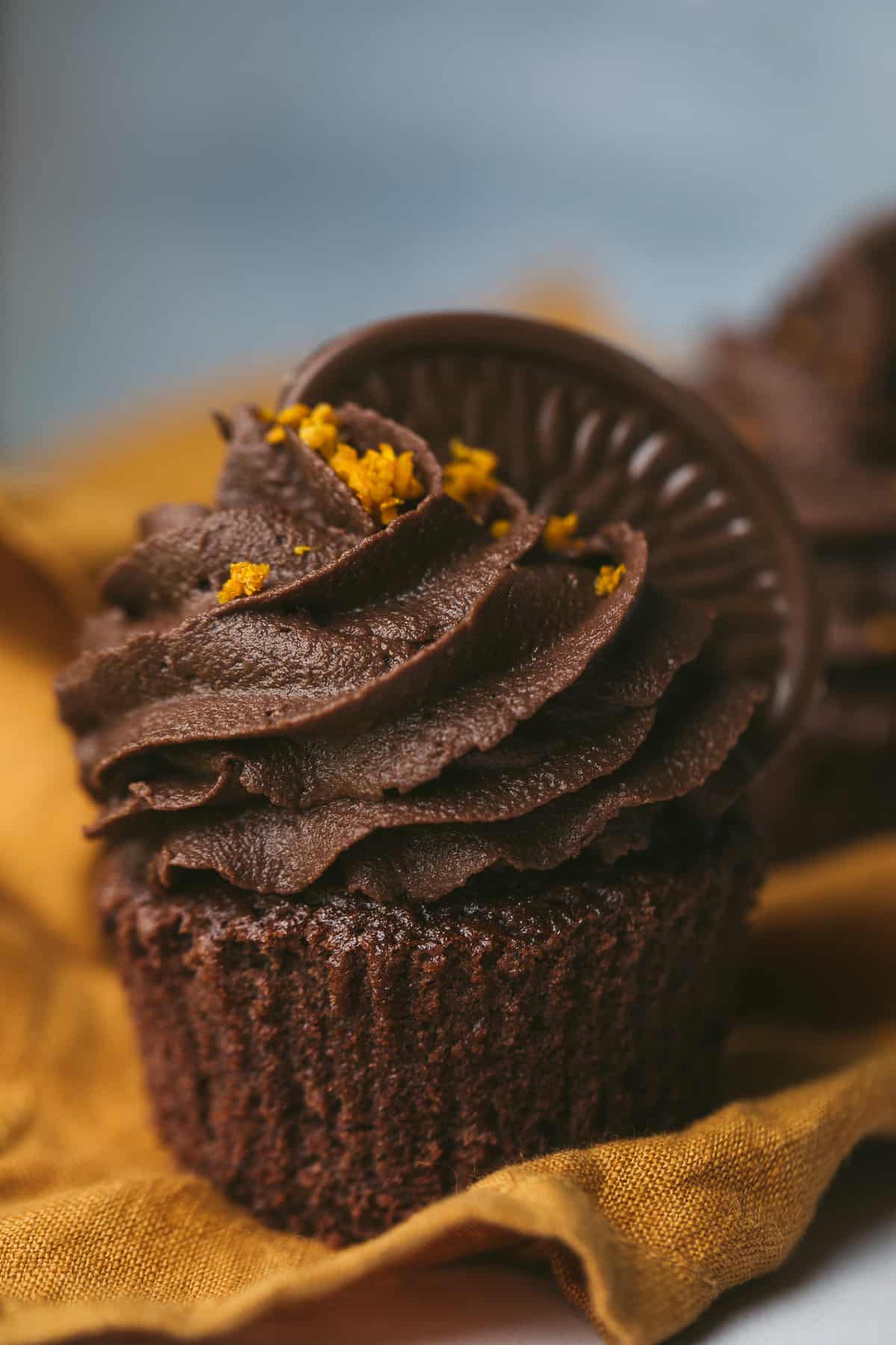 A chocolate orange cupcake with a buttercream made from a dark Terry's chocolate orange. The cupcake is topped with a segment of chocolate orange and has been sprinkled with freshly grated orange zest. 