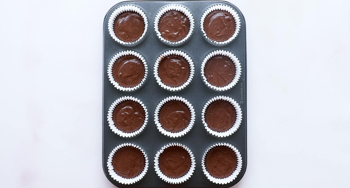A 12 hole baking tin with 12 cupcake cases filled with cupcake mixture. 