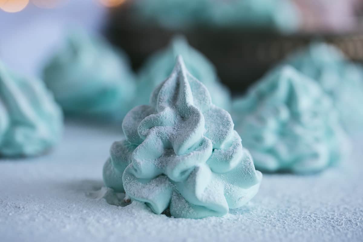 A green meringue in the shape of a christmas tree. It has been covered in icing sugar to look like snow. 